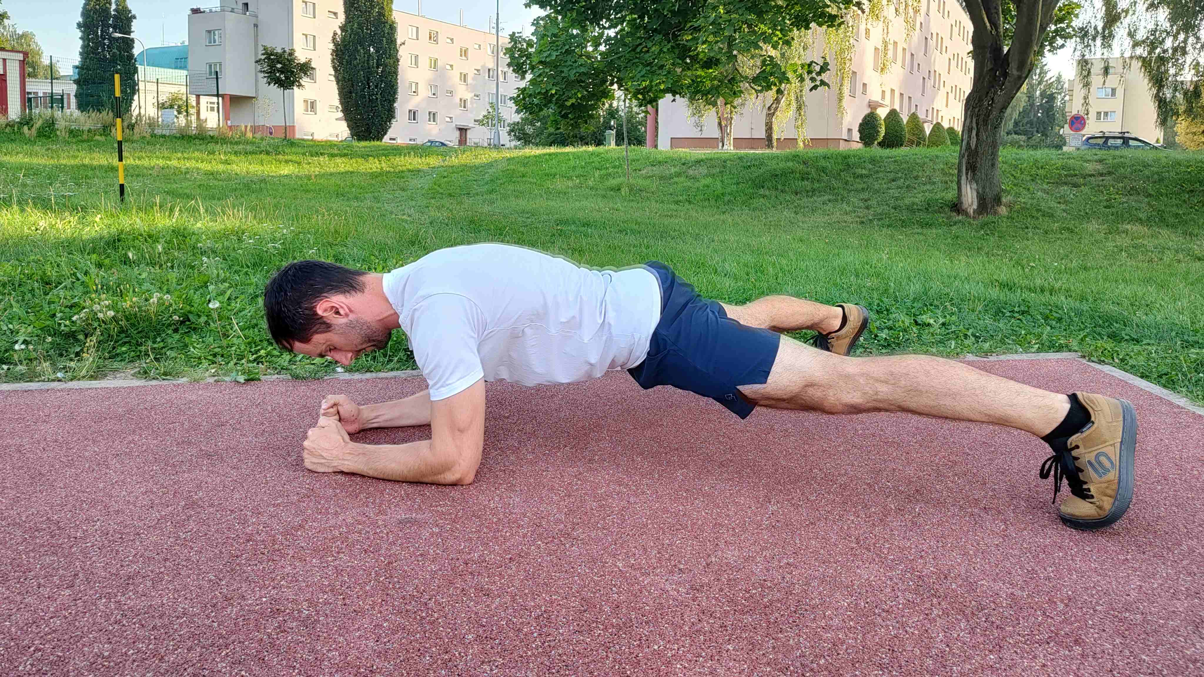 Muž v parku cvičí plank s rozkročenýma nohama.